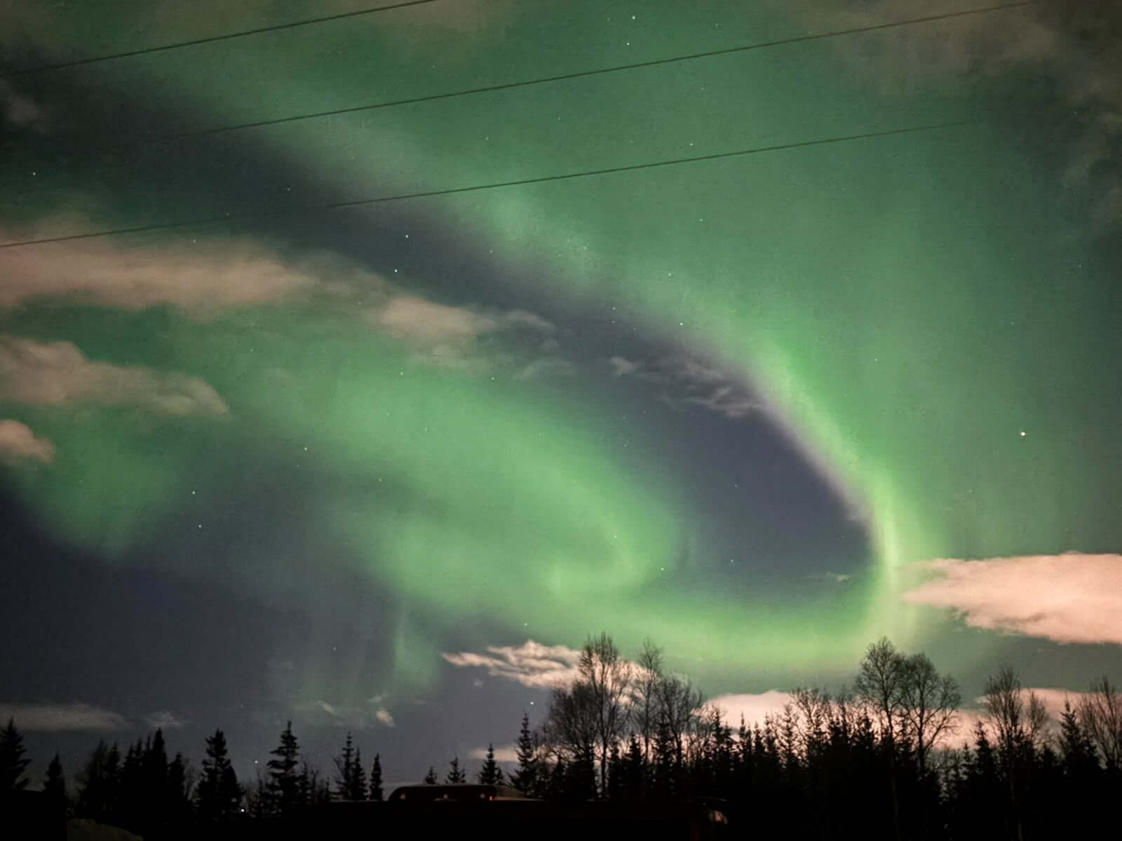 Aurora arc over a forest under drifting clouds