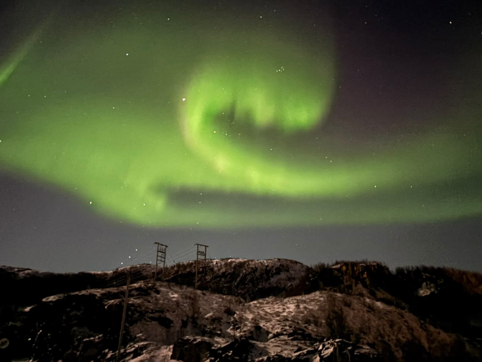 Swirling green aurora above a rocky winter hill